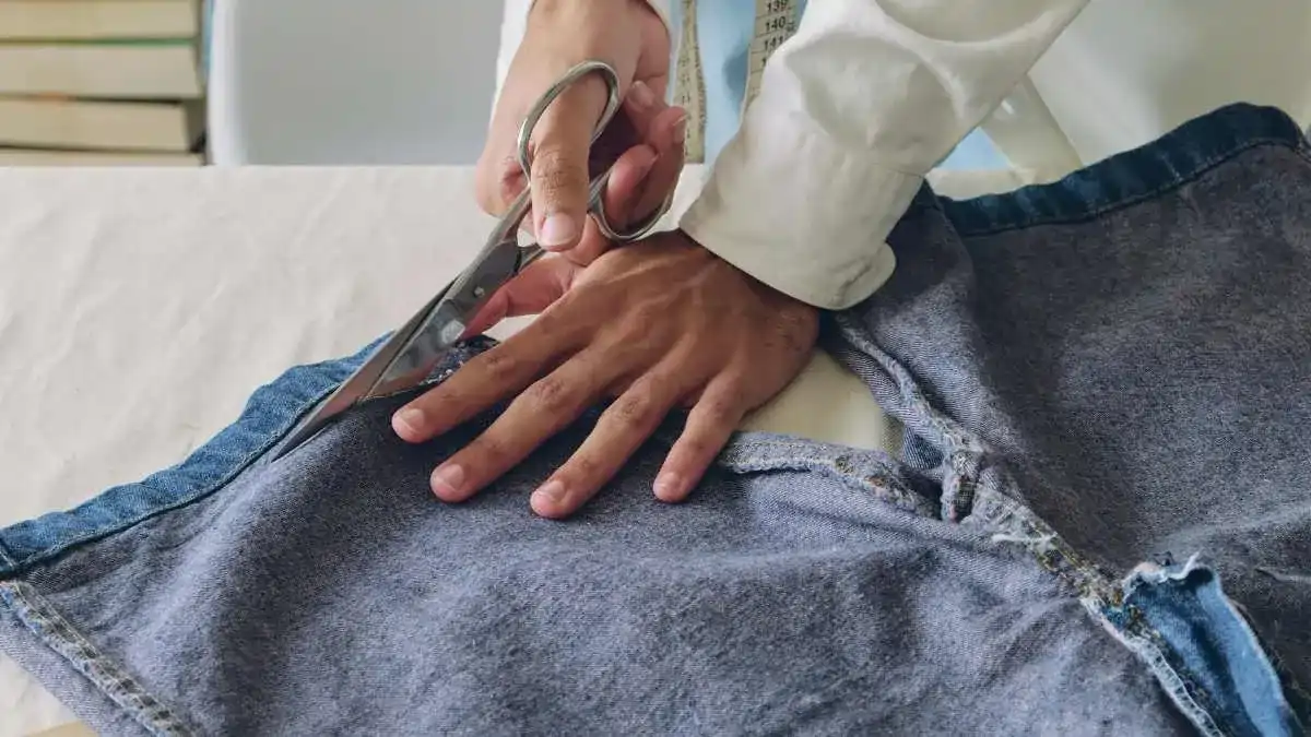 Mãos cortando uma calça  para fazer Upcycling e o passo a passo no blog Conversa pronta